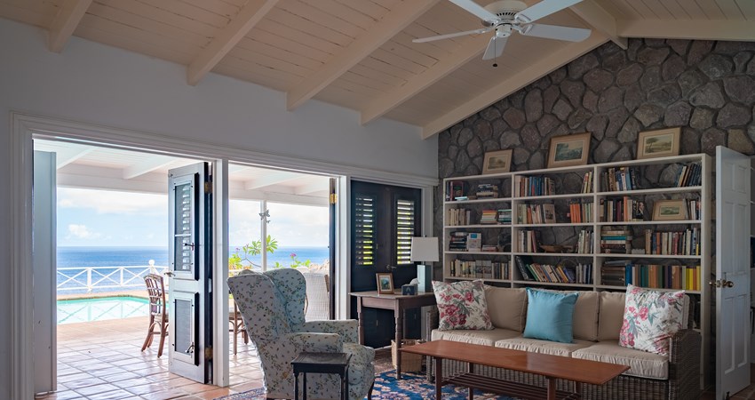 Living room with a well stacked book shelf and two open doors overlooking the ocean