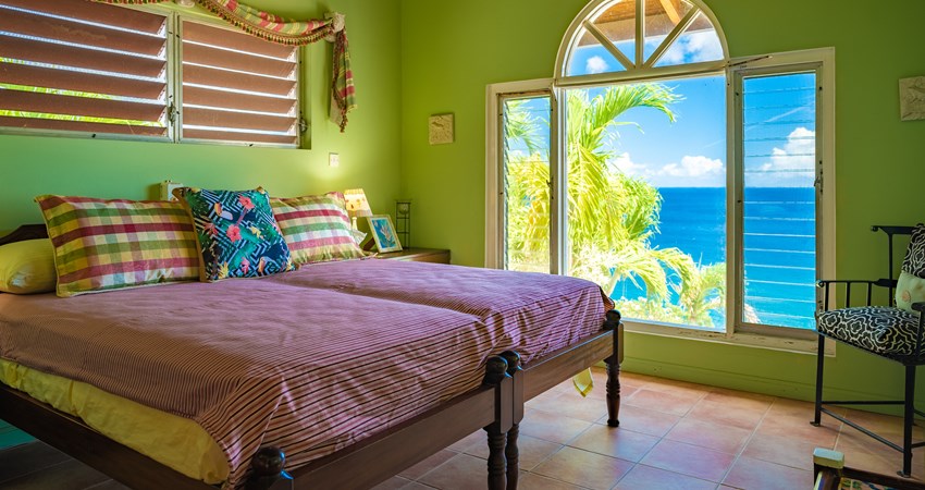 Green bedroom with a window overlooking the oceon